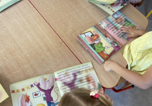 Dzieci przy stolikach oglądają sprezentowane książki