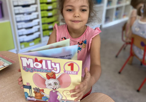 Dziewczynka siedząca przy stoliku z książką "Myszka Molly" w rękach