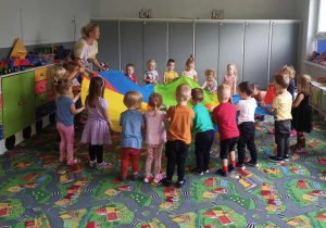 Sala Przedszkola. Dzieci wraz z nauczycielem uczestniczą w zabawie z chustą animacyjną i balonami.