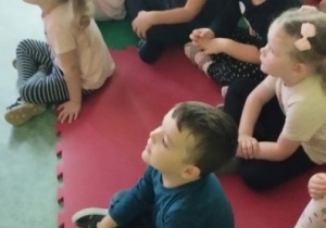 Dzieci siedzą w sali gimnastycznej i z zaciekawieniem oglądają przedstawienie.