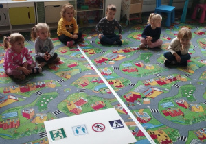 Sala przedszkolna. Dzieci siedzą w kole na dywanie i poznają różnego rodzaju znaki informacyjne.