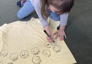 dziewczynka rysuje uśmiechniętą buźkę na koszulce