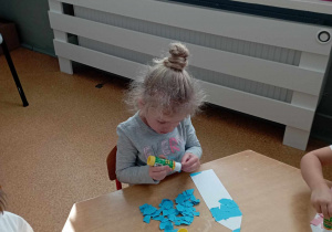 Dziewczynka smaruje klejem kawałek papieru kolorowego, którym wykleja szablon kredki