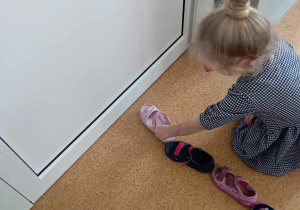 Dziewczynka ustawia swój but przed butami innych dzieci podczas andrzejkowej zabawy