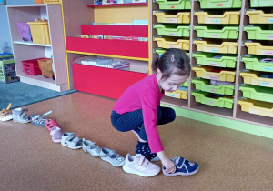 Dziewczynka ustawia swój but przed butami innych dzieci w andrzejkowej zabawie