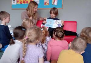 Chłopiec pokazuje dzieciom ilustracje w książce, którą czyta dzieciom jego mama