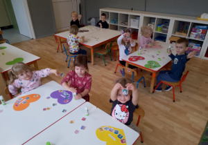 Sala przedszkolna. Dzieci siedzą przy stoliku i wyszukują wśród obrazków na stole, wskazany przez nauczyciela obrazek, ilustrujący poszczególne prawa dziecka.