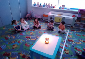 Sala przedszkolna. Dzieci siedzą na dywanie dookoła stołu, na którym stoi świeca.