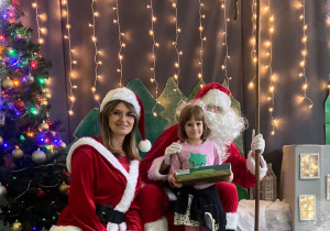 Dziewczynka z prezentem w ręku pozująca do zdjęcia ze Świętym Mikołajem i Panią Mikołajową