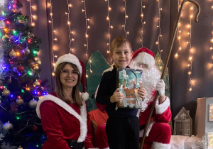 Chłopiec z prezentem w ręku pozująca do zdjęcia ze Świętym Mikołajem i Panią Mikołajową