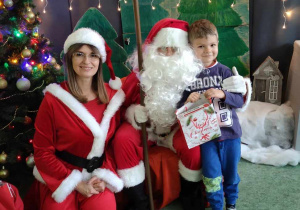 Chłopiec pozuje do zdjęcia z Mikołajem i Mikołąjką na tle świątecznej dekoracji