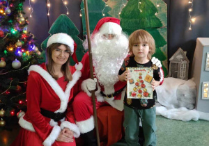 Chłopiec pozuje do zdjęcia z Mikołajem i Mikołajką na tle świątecznej dekoracji