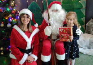 Dziewczynka pozuje do zdjęcia z Mikołajem i Mikołąjką na tle świątecznej dekoracji