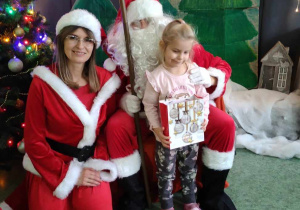 Dziewczynka pozuje do zdjęcia z Mikołajem i Mikołajką na tle świątecznej dekoracji