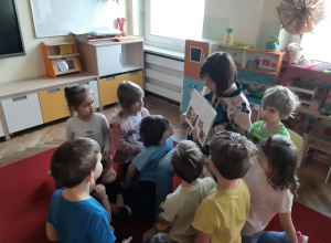 Dzieci z uwagą słuchają książki czytanej przez jedną z mam