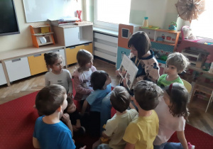 Dzieci z uwagą słuchają książki czytanej przez jedną z mam