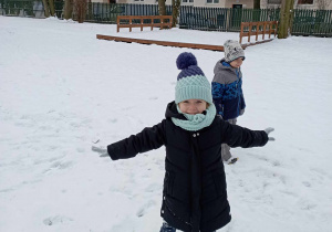 Dziewczynka pozuje do zdjęcia na tle zaśnieżonego ogrodu przedszkolnego