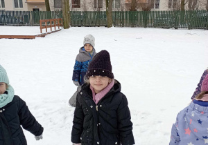 Dziewczynka pozuje do zdjęcia na tle zaśnieżonego ogrodu przedszkolnego