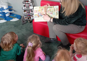 Dzieci przyglądają się ilustracjom w książce czytanej przez jedną z mam