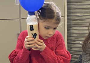 dziewczynka słucha jak pracują drożdże w butelce z nałożonym balonem