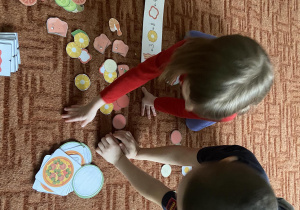 Chłopiec z dziewczynką na dywanie układają składniki do pizzy