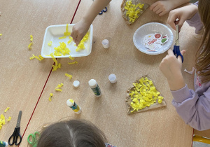 Dzieci przy stoliku wyklejają kawałek pizzy żółtą bibuła - praca plastyczna