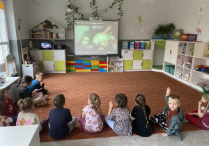 Dzieci na dywanie przed tablicą interaktywną oglądają filmik dydaktyczny o powstawaniu pizzy