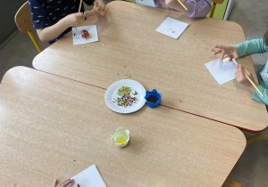 Dzieci przy stolikach ozdabiają masę plastyczną w kształcie pączków farbą i posypką