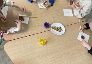 Dzieci przy stoliku ozdabiają pączki z masy plastycznej