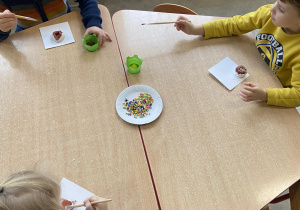 Dzieci przy stolikach malują farbami pączki z masy plastycznej