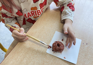 Dziewczynka maluje brązową farbą uformowanego przez siebie pączka