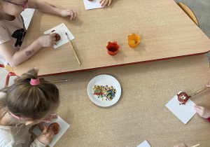 Dzieci przy stoliku przygotowują pracę plastyczną pączki z masy plastycznej