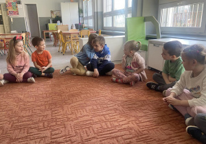 Dzieci w kole na dywanie grają w "Głuchy telefon" - przekazując hasło Kocham Cię