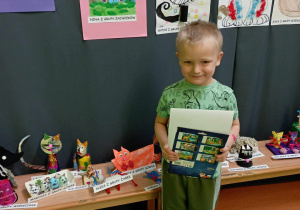 Chłopiec pozuje do zdjęcia na tle wystawy prac plastycznych
