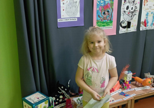 Dziewczynka pozuje do zdjęcia na tle wystawy prac plastycznych