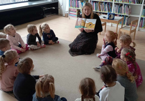 Dzieci oglądają ilustrację w książce czytanej przez panią bibliotekarkę