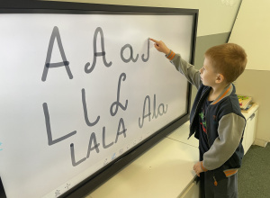 chłopiec pisze litery na ekranie multimedialnym