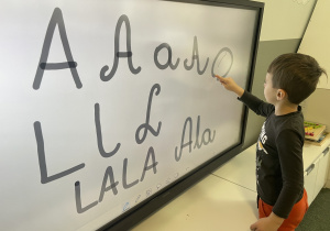 chłopiec pisze litery w pozycji wertykalnej na ekranie multimedialnym