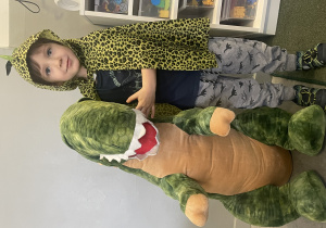 chłopiec w pelerynie dinozaura pozuje z wielkim pluszowym dinozaurem