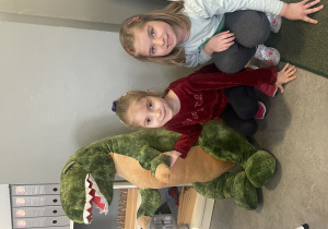 dziewczynki pozują z pluszowym dinozaurem
