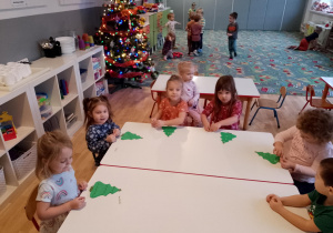 Sala przedszkolna. Dzieci siedzą przy stoliku i malują farbami świąteczne ozdoby.