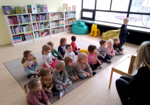 Biblioteka ,,Ferment". Dzieci siedzą na dywanie, słuchają opowieści w formie teatru Kamishibai.