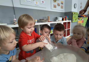 Sala przedszkolna. Dzieci dodają składniki do miski.