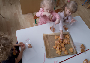 Sala przedszkolna. Dzieci siedzą przy stoliku i pakują ciasteczka.