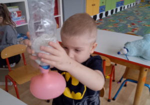 Sala przedszkolna. Chłopiec przesypuje mąkę z plastikowej butelki do balona.