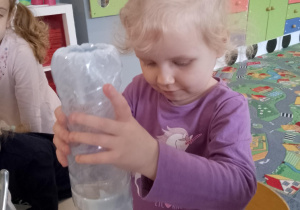 Sala przedszkolna. Dziewczynka przesypuje mąkę z plastikowej butelki do balona.