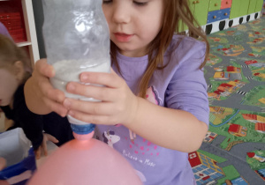 Sala przedszkolna. Dziewczynka przesypuje mąkę z plastikowej butelki do balona.