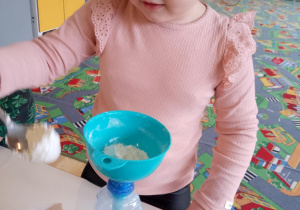 Sala przedszkolna. Dziewczynka za pomocą łyżki i lejka, wsypuje mąkę do plastikowej butelki.