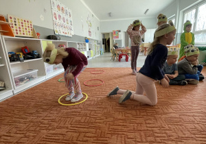 Dzieci przeskakujące stylem żabki po rozłożonych obręczach na dywanie