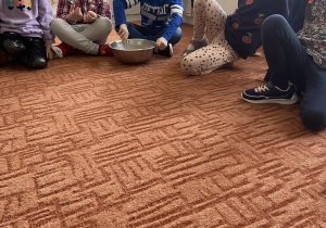 Dzieci siedzące na dywanie, chłopiec miesza ciasto w metalowej misce na babeczki